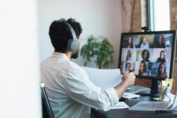 While telecommuting from his home, a young businessman gives a presentation during a video conference.