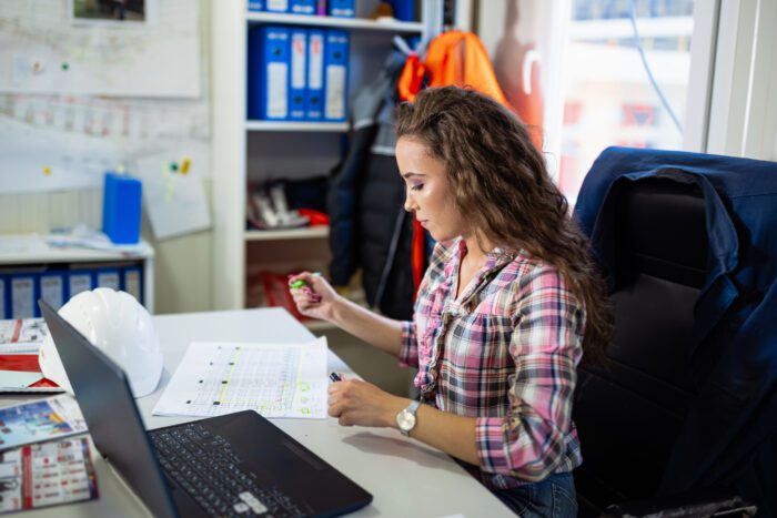 A young Caucasian female civil engineer is checking the new project plans, while sitting at her desk.